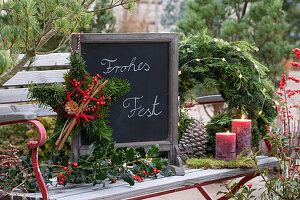 Star made of fir branches, holly branch and slate board with Christmas greeting on garden bench