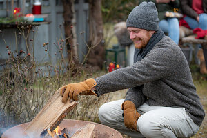 Mann legt Holzscheit in die Feuerschale
