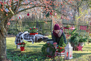 Frau dekoriert weihnachtlichen Sitzplatz mit Laterne, Dekopilzen und Kranz im Garten