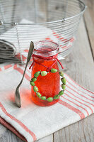 Blackcurrant syrup in a glass with a wreath of poppy pods and a silver spoon on a tea towel