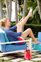 Blonde woman sitting on an outdoor armchair and massaging her legs
