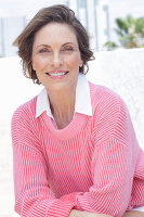 Frau in pinkfarbenem Pullover und weißem Hemd am Strand