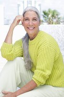 Gray-haired woman in a green-yellow knit sweater and light-colored trousers