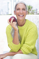 Grauhaarige Frau mit einem Apfel in grüngelbem Strickpullover