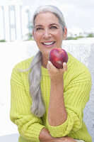 Grauhaarige Frau mit einem Apfel in grüngelbem Strickpullover