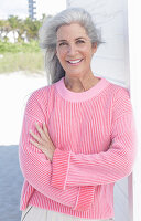 Grauhaarige Frau in pinkfarbenem Pullover am Strand