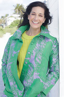 Reife, dunkelhaarige Frau in grünem Mantel und grüngelbem Strickpullover