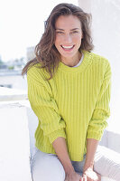 A happy, long-haired woman wearing a green-yellow knitted jumper and white trousers
