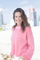 A happy, long-haired woman wearing a pink jumper and white trousers