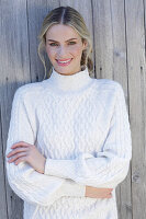Young blonde woman in a white knitted jumper in front of a board wall