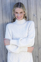 Young blond woman in white knitted jumper in front of board wall