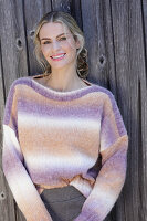 Young blond woman in knitted jumper with colour gradient in front of board wall