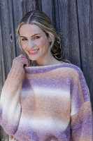 Young blond woman in knitted jumper with colour gradient in front of board wall