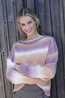 Young blond woman in knitted jumper with colour gradient in front of board wall