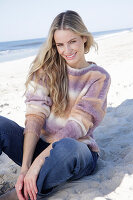 Young blond woman in knitted jumper with colour gradient and jeans by the sea