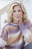 A mature blonde woman wearing a knitted colour gradient jumper