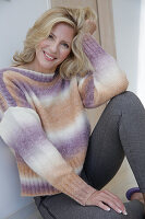 Mature blonde woman in knitted jumper with colour gradient and grey leggings