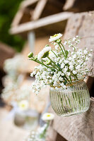 Weisse Blumen in einer Glasvase hängen an einer Holzpalette