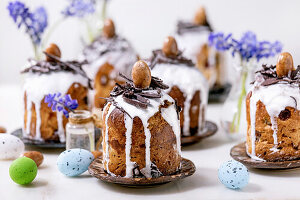 Homemade traditionla small Easter kulich cakes with chocolate nests and eggs on plates decorated with muscari flowers