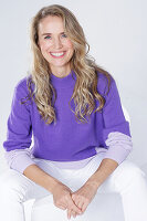 Blond woman wearing a purple sweater and white trousers