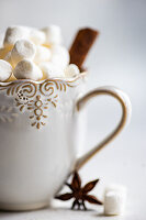 Cup of hot chocolate and mini marshmallow with cinnamon stock and anise star on white concrete background
