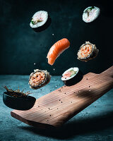 Verschiedene Sushi und ein Schälchen mit Sojasauce, fliegend über Holzbrett