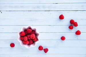 Raspberries in a small bowl and on a white wooden background