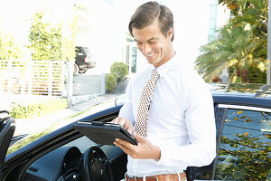 Junger Geschäftsmann mit Tablet in der Hand steht neben Auto