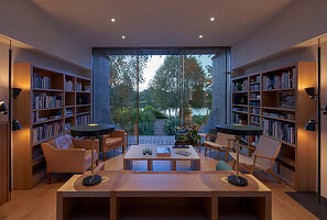 Illuminated living room with bookshelves and seating, view of river through glass patio door
