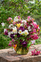 Blumenstrauss aus Narzissen (Narcissus), Tulpen (Tulipa) und Zierapfelblüten auf Gartenmauer