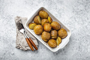 Hasselback potatoes with herbs in white ceramic casserole