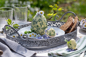 Kräuterbutter in Eiform mit Schnittlauch, Petersilie, Knoblauch, Thymian, dekoriert mit Gänseblümchen auf Silbertablett