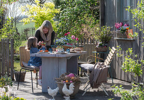 Mutter und Kind beim Osterfrühstück am gedeckten Tisch auf der Terrasse