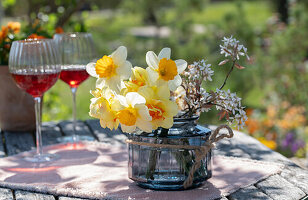 Blumenstrauß aus Narzissen (Narcissus) und blühende Zweige der Felsenbirne (Amelanchier) in Vase und Weingläser auf Tisch