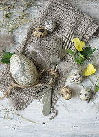 Deco egg, quail eggs, feather, and cutlery on knitted napkin