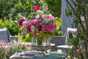 Bouquet of peonies with goutweed and lady's mantle in glass vase on patio table