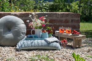 Bouquet and jug with strawberries on a cushion in the garden, next to it a bench with drinks
