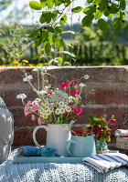 Sommerlicher Blumenstrauß und Krug mit Erdbeeren auf Bodenkissen im Garten