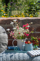 Sommerlicher Blumenstrauß und Krug mit Erdbeeren auf Bodenkissen im Garten