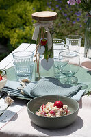 Salat, Gläser, Glasflasche und Servietten auf Tisch fürs Sommerfest im Garten