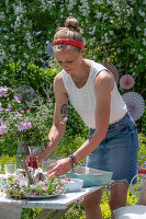 Junge Frau deckt Tisch fürs Sommerfest im Garten