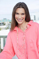 Young woman in salmon coloured shirt with pearl necklace
