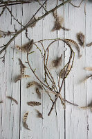 Herz aus knospigen Zweigen geformt und Feder auf Holztisch