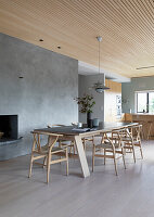 Long dining table with classic chairs in front of concrete wall and fireplace