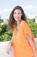 A cheerful young woman wearing an orange summer blouse with a necklace