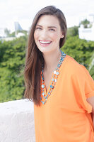 A cheerful young woman wearing an orange summer blouse with a necklace