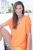 A cheerful young woman wearing an orange summer blouse with a necklace