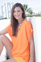 A cheerful young woman wearing an orange summer blouse with a necklace