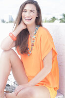 A cheerful young woman wearing an orange summer blouse with a necklace