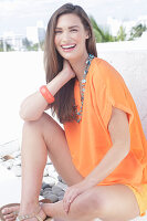 Fröhliche junge Frau in orangefarbener Sommerbluse mit Halskette